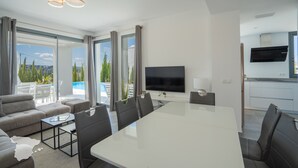 Un salon moderne avec une grande table blanche, des canapés gris et un téléviseur à écran plat.