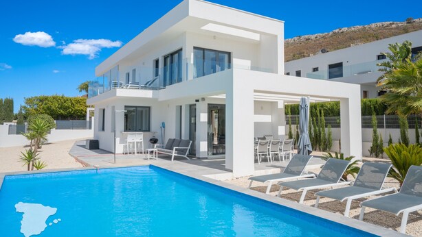Une maison moderne à deux étages, dotée d’une piscine, d’un espace de détente extérieur et offrant une vue sur un paysage montagneux.