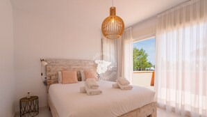 Une chambre à coucher avec une tête de lit en bois, un lit recouvert de draps blancs, une lampe de chevet et une vue sur l’extérieur.