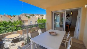 Een balkon met een tafel en stoelen, uitzicht op gebouwen en een heldere lucht.