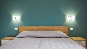 A bedroom with a wooden headboard, a white patterned bedspread, and two bedside tables with wall-mounted lights. - 1 bedroom beautiful apartment in Siracusa (Siracusa)