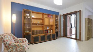 A room with a large wooden bookshelf, a patterned armchair, and a sliding glass door leading to an outdoor area. - 1 bedroom beautiful apartment in Siracusa (Siracusa)