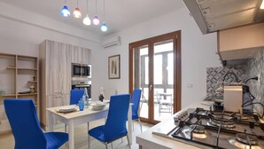 A modern kitchen with a gas stove, a dining table with blue chairs, and a view through a glass door to an outdoor patio. - 1 bedroom beautiful apartment in Siracusa (Siracusa)