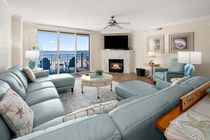 A living room with a sofa, a fireplace, a television, and a balcony with a view of the ocean.