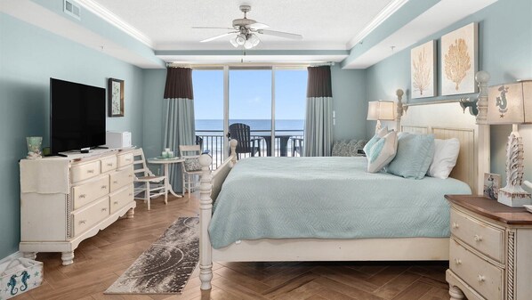 Ein Schlafzimmer mit Bett, Schminktisch, Fernseher und einem Balkon mit Meerblick.