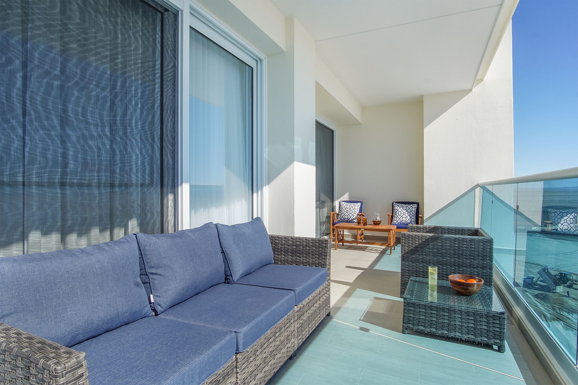 Ein Balkon mit blauer Couch, Korbmöbeln und einem Glastisch mit Schüssel und Getränken.