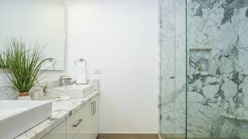 A modern bathroom with a marble vanity, a glass shower enclosure, and a potted plant.