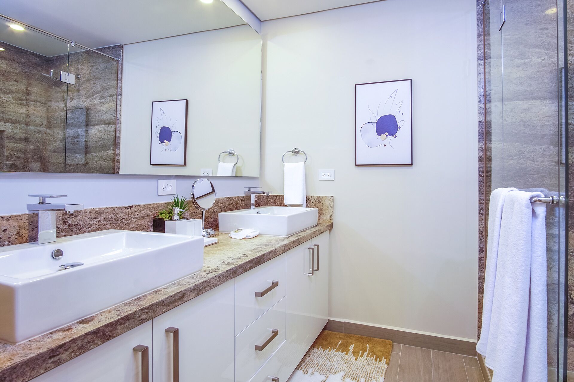 Un baño moderno con dos lavamanos, un espejo grande y obras de arte en las paredes.