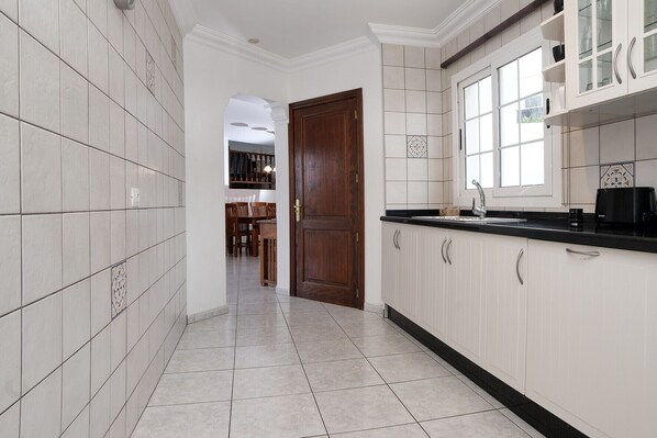 A kitchen with white cabinets, a black countertop, and a wooden door. - Casa Paraíso • Jacuzzi, A/C & BBQ (Tías)