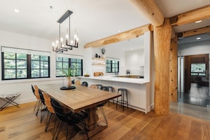 A modern kitchen with a wooden dining table, black chairs, and a pendant light.