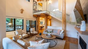Relax in the spacious living area with plush sofas and a large coffee table, surrounded by large windows offering views of the surrounding landscape.