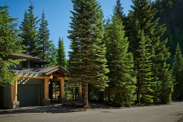 Un chalet doté d’une entrée couverte, entouré de grands arbres à feuilles persistantes.