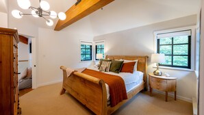 A bedroom with a wooden bed, two windows, a nightstand, and a ceiling light fixture.