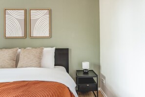 A neatly made bed with a striped blanket, a dark headboard, and two pillows. There is a small bedside table with a lamp and a framed picture above it.