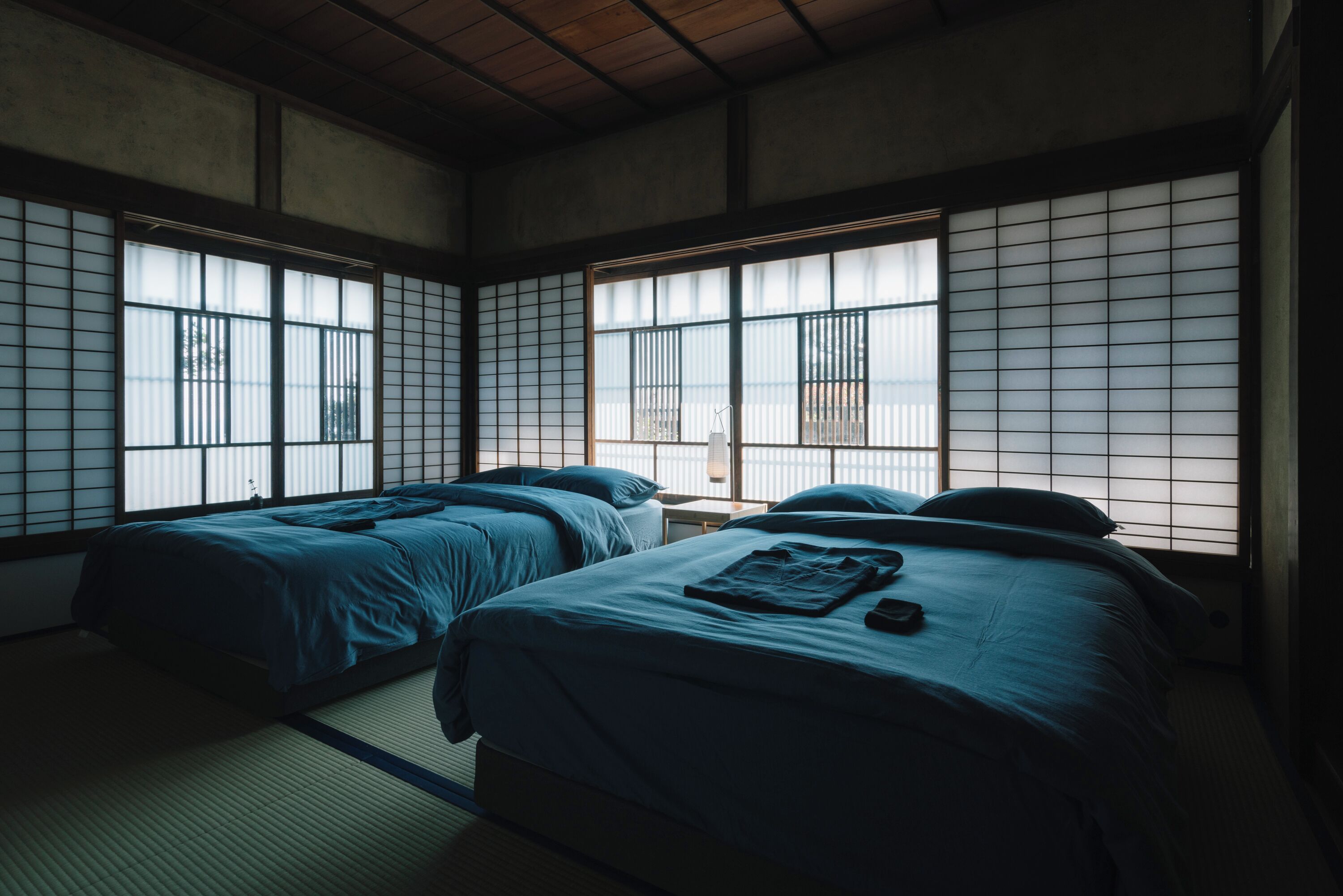 A traditional Japanese-style room with tatami flooring, two beds with blue bedding, and shoji screens.