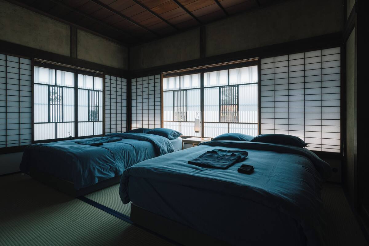 Um quarto tradicional japonês com tatames, duas camas com roupa de cama azul e biombos shoji.