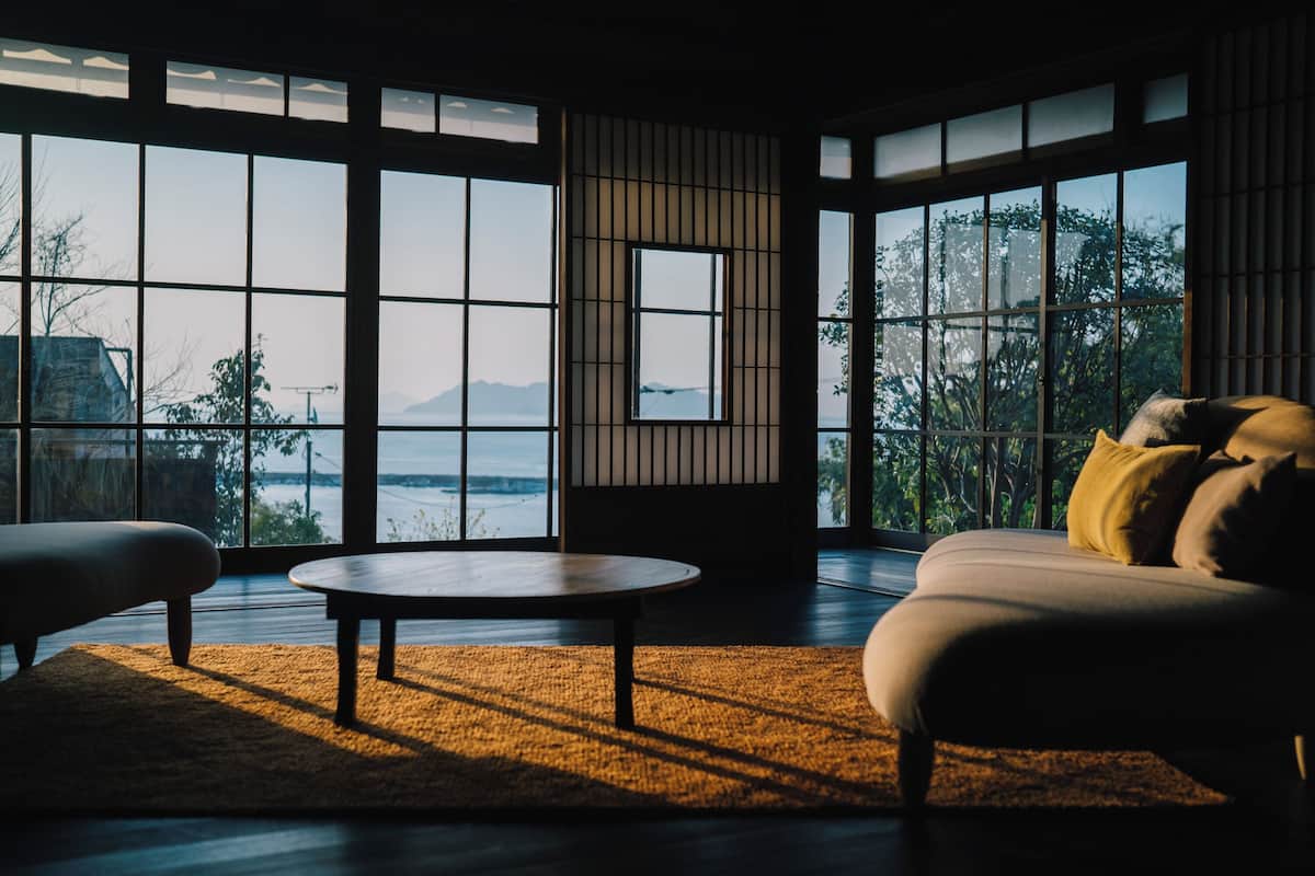 Quarto com janelas amplas, sofá, mesa redonda e vista para o exterior.