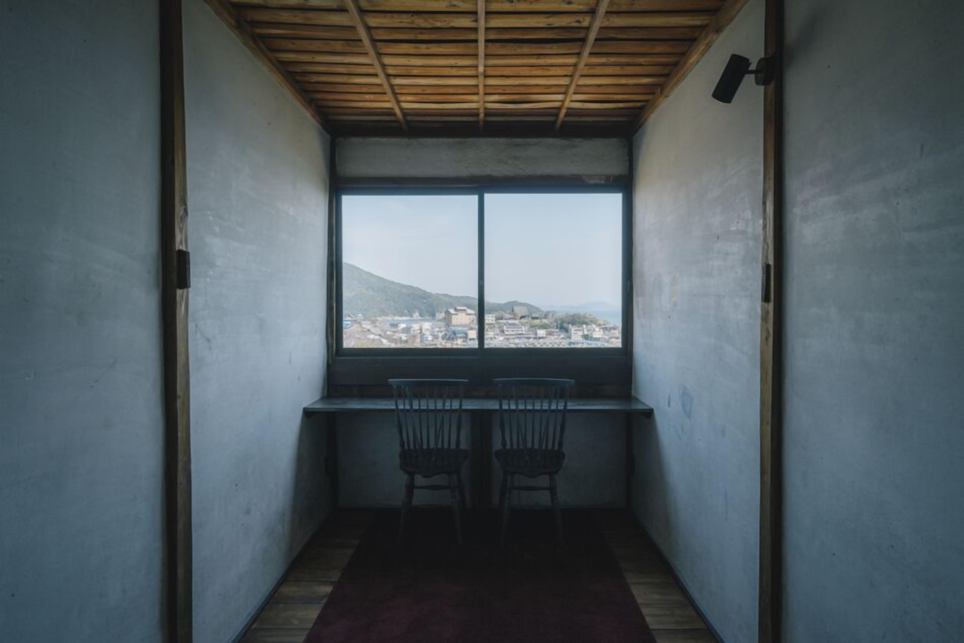 A room with a large window, two chairs, a desk, and a wooden ceiling.