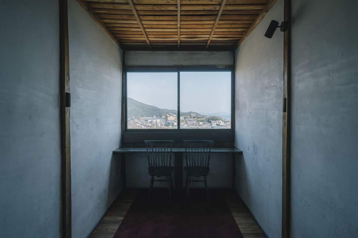 A room with a large window, two chairs, a desk, and a wooden ceiling.