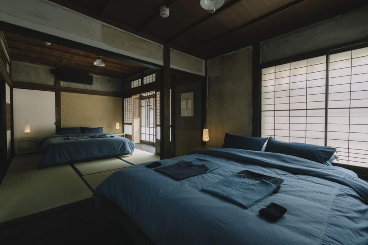 A traditional Japanese-style room with tatami flooring, a large bed with blue bedding, a small table, and a sliding door.