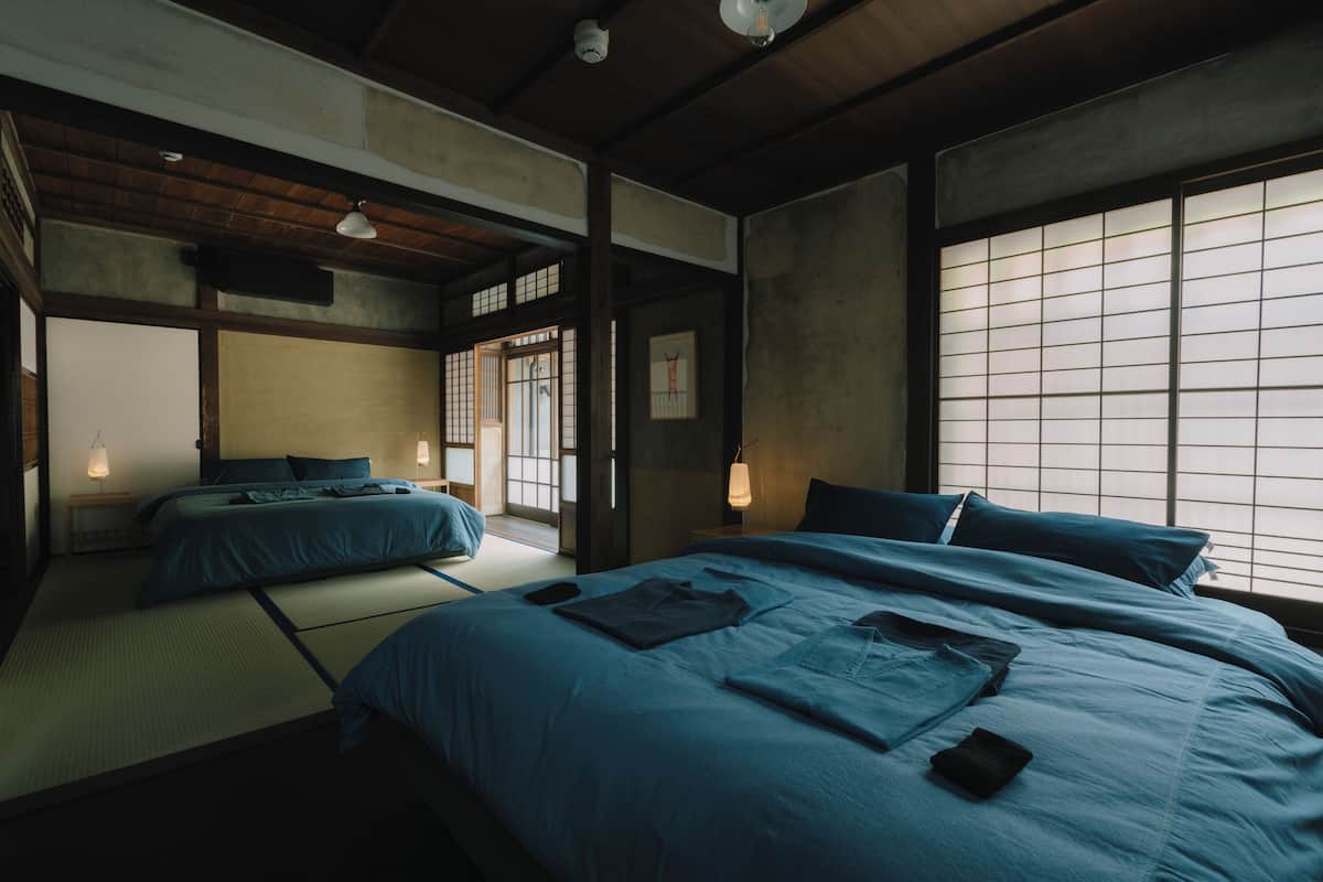 A traditional Japanese-style room with tatami flooring, two beds with blue bedding, and a shoji screen door.