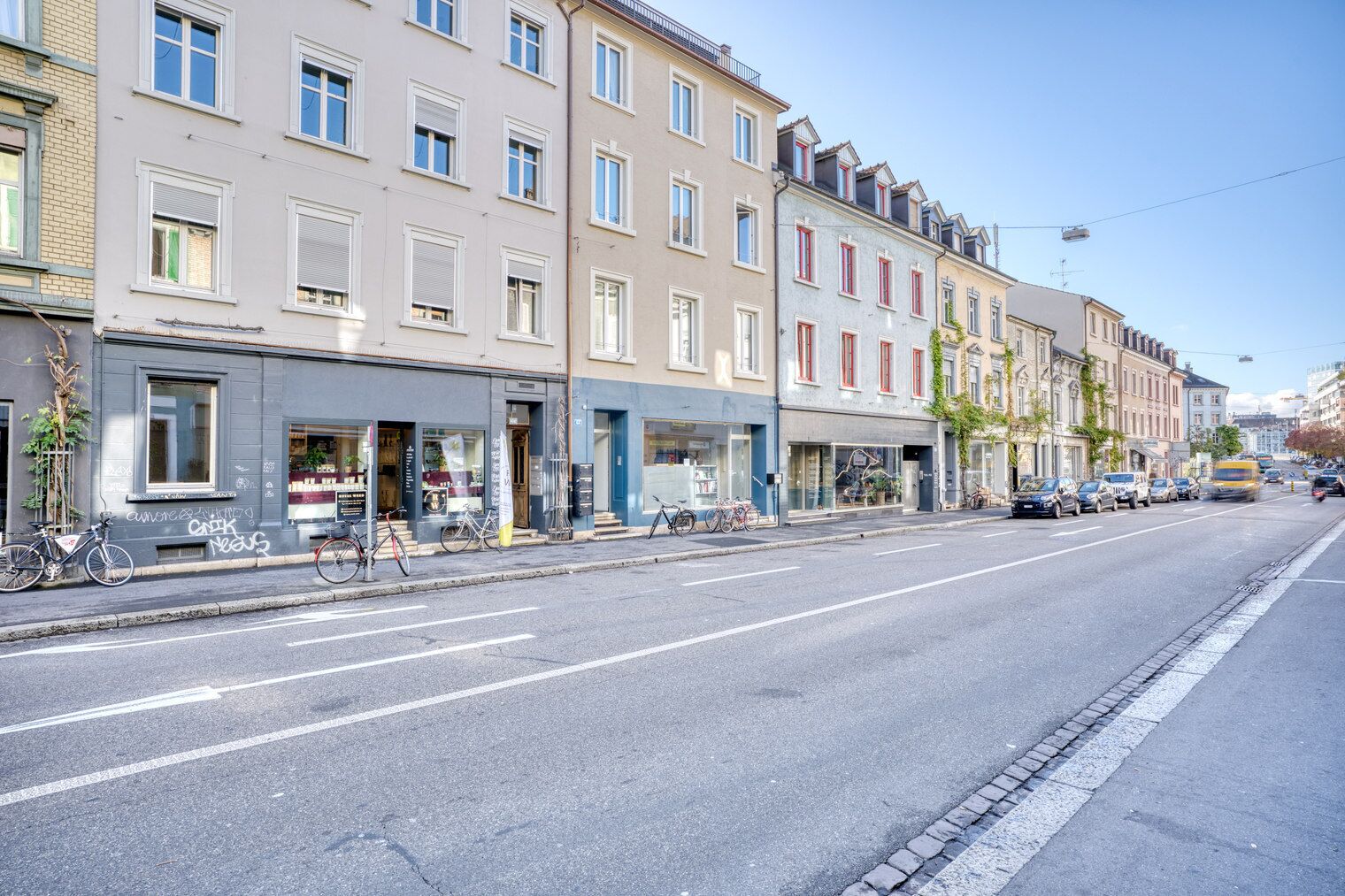 Katu, jonka varrella on korkeita kerrostaloja, pyöriä on pysäköitynä kadun varteen ja autot ajavat sillä.