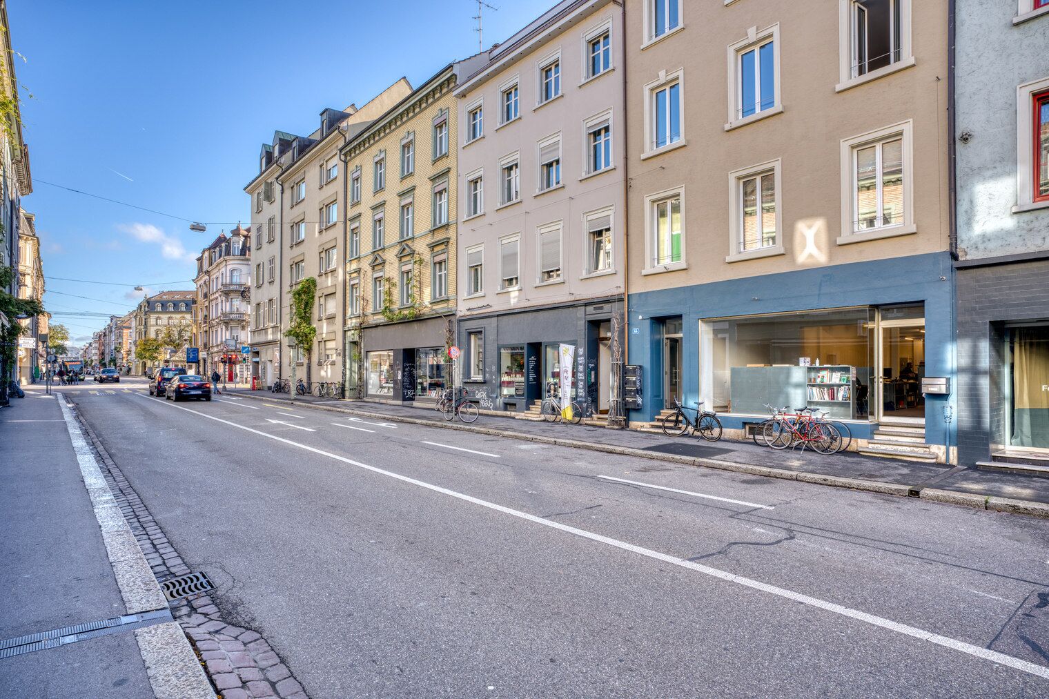 A street with buildings, a clear sky, and parked bicycles.