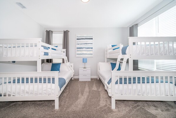 A bedroom with bunk beds, a nightstand, a lamp, and a window with blinds.