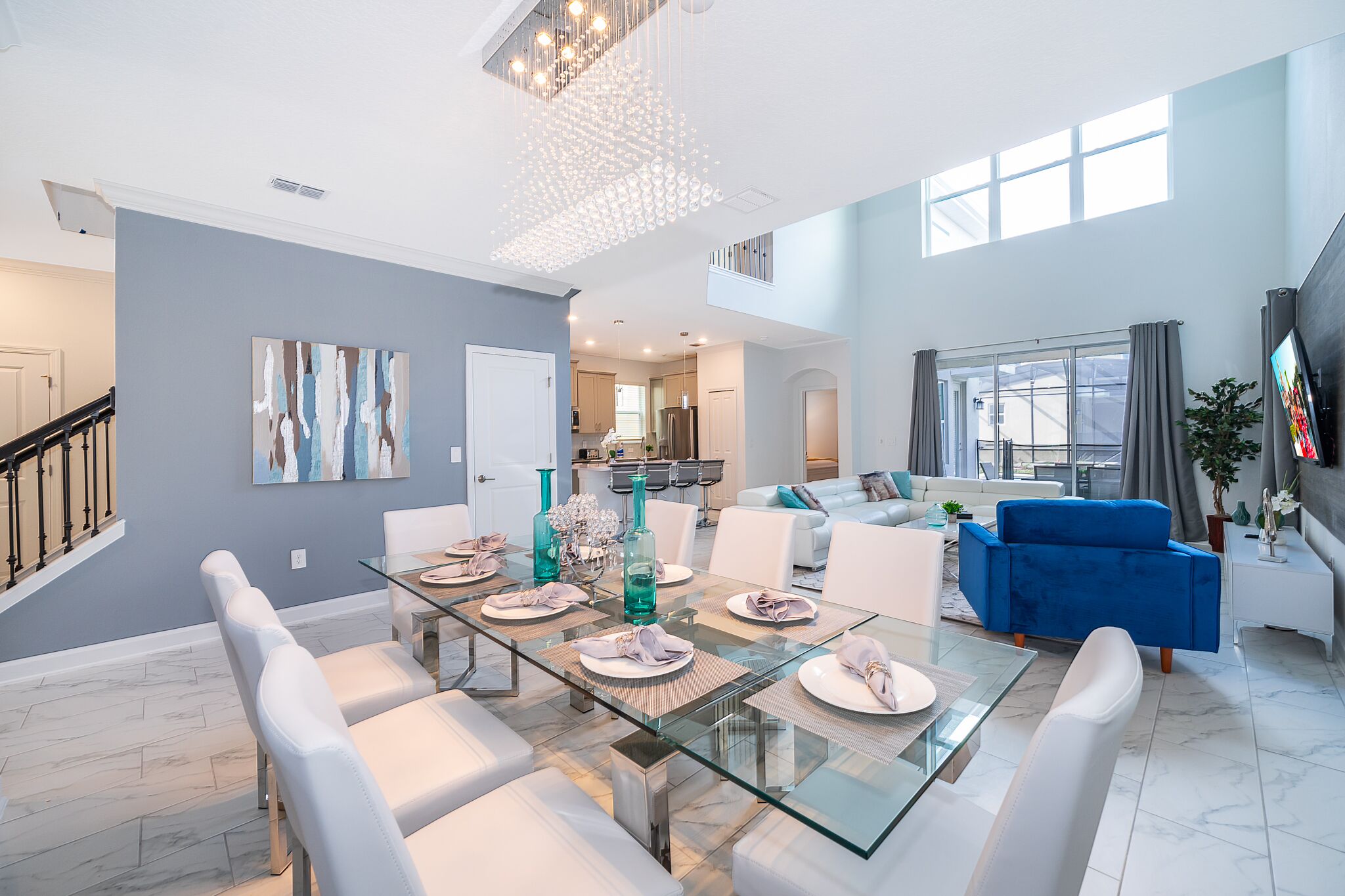 A spacious living area with a glass dining table, white sofas, and a blue armchair.