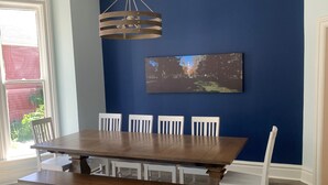 Uma sala de jantar com uma grande mesa de madeira, cadeiras brancas e um lustre.