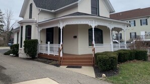 Uma casa de dois andares com varanda em volta, chaminé e porta da frente.