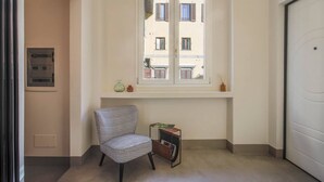 Ein Zimmer mit Fenster, einem Stuhl, einem kleinen Tisch und einer Tür.