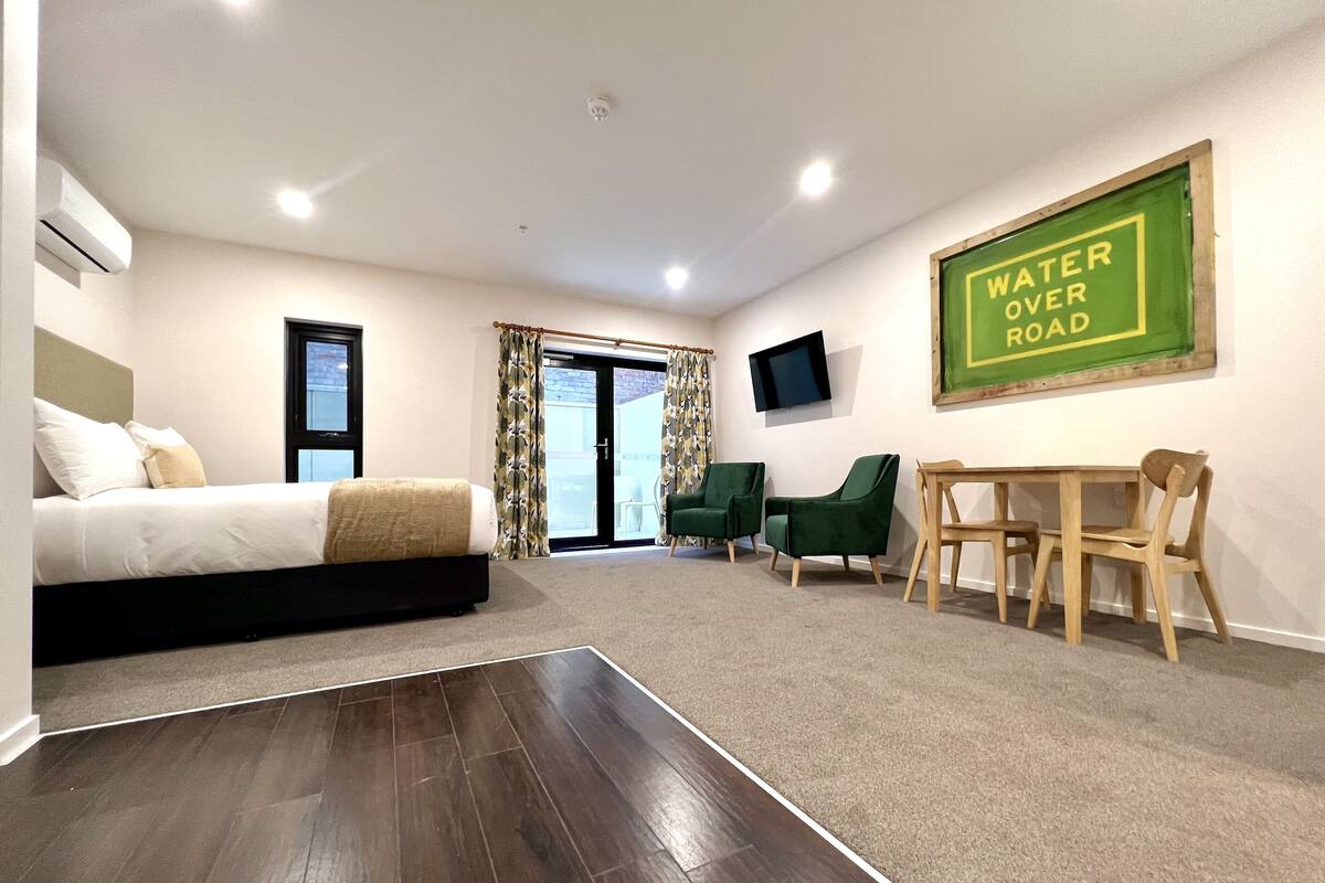 Une chambre d’hôtel moderne équipée d’un lit, d’un bureau, de deux chaises, d’une télévision et d’un panneau indiquant « Water Over Road ».