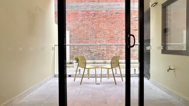 A view from an interior space to an outdoor area with a brick wall, two chairs, and a table. - Sixty Six Boutique Apartments (North Hobart)
