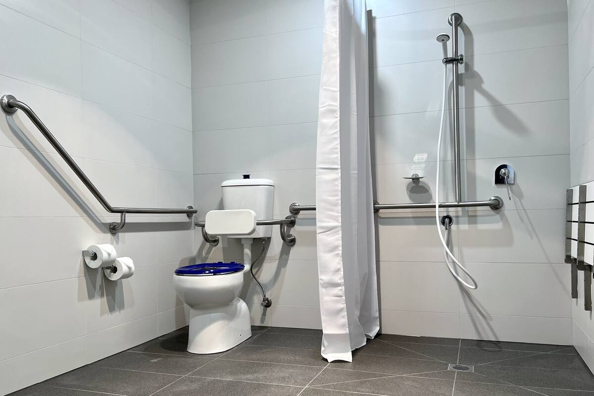 Une salle de bain équipée de toilettes, de barres d’appui, d’une douche et d’un rideau.