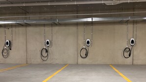 An empty parking garage with four charging stations, marked parking spaces, and a concrete floor. - Sixty Six Boutique Apartments (North Hobart)