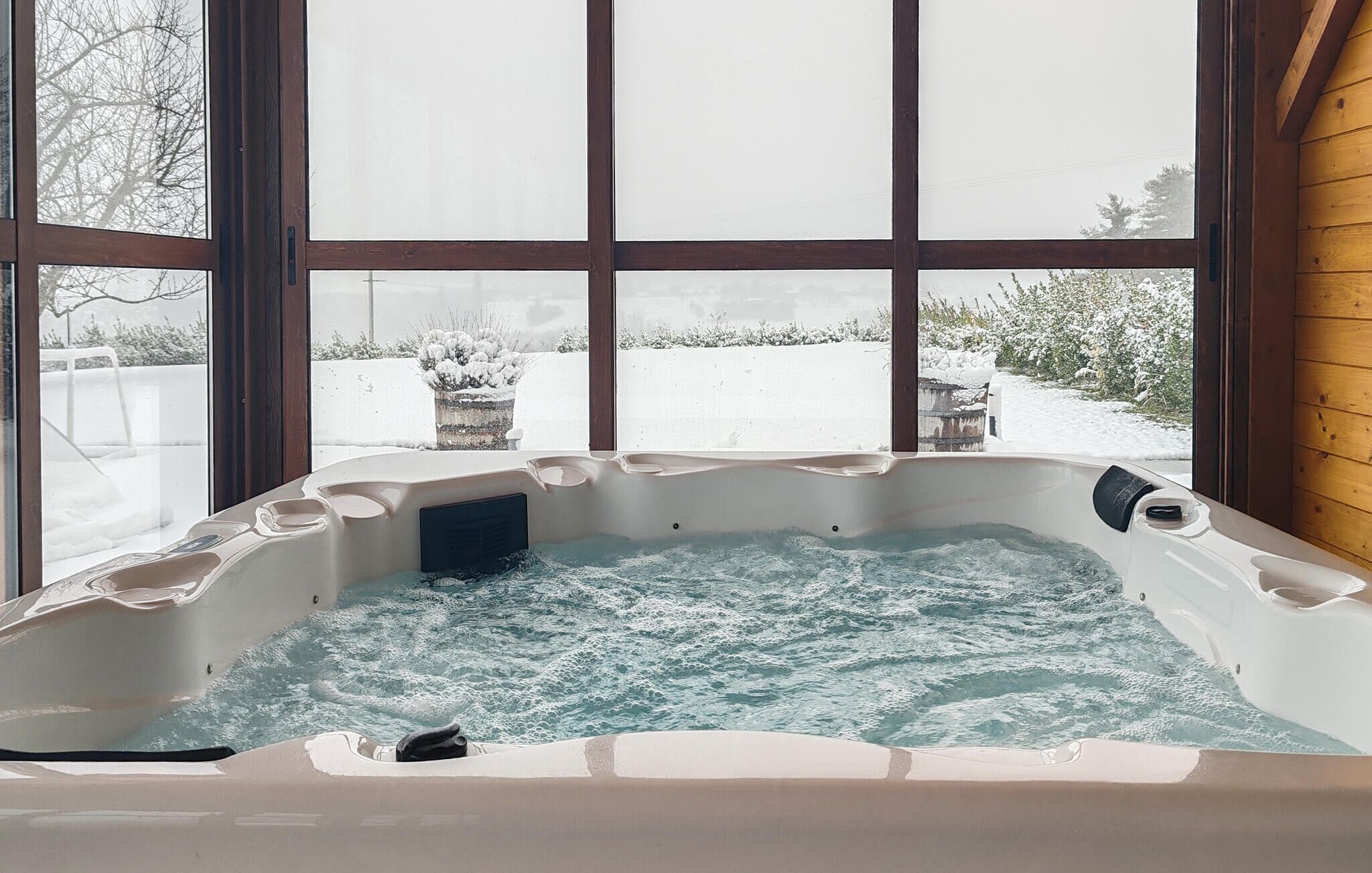 A hot tub with a view of a snowy landscape through large windows.