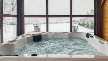 A hot tub with a view of a snowy landscape through large windows.