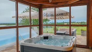 A hot tub in a covered outdoor area with a view of a pool and greenery.