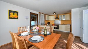 Un coin repas avec une table en bois dressée pour quatre personnes, une cuisine en arrière-plan et un réfrigérateur sur la droite.