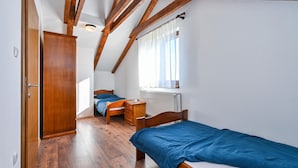 Une petite pièce bien éclairée, avec des poutres en bois au plafond, un lit, un bureau et une armoire.