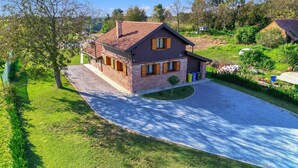 Une maison à deux étages, avec une façade en briques et un toit recouvert de tuiles, entourée d’une pelouse bien entretenue et d’arbres.