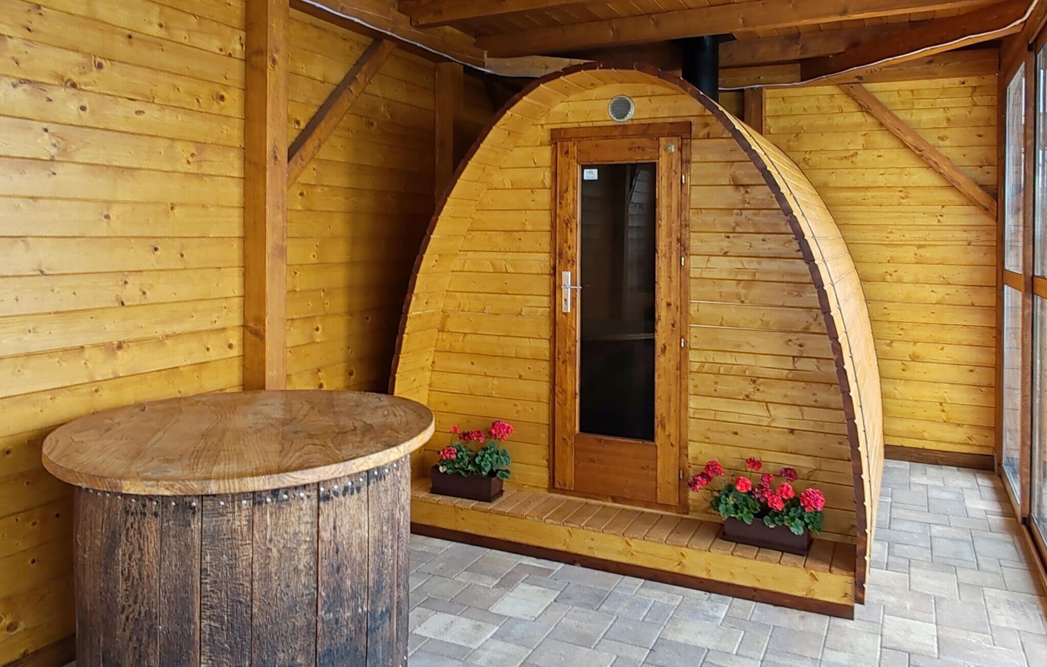 A wooden cabin with a curved entrance, a wooden table, and flower boxes on the porch.