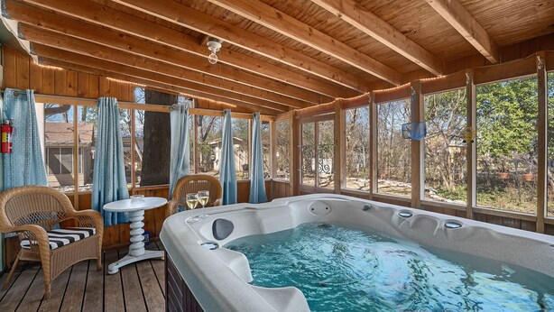 A wooden deck with a hot tub, wicker chairs, and a table with a glass. - Hein House | Hot Tub | Shared Pool (Fredericksburg)