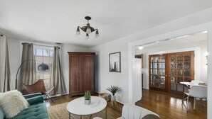 A living room with a sofa, chairs, a coffee table, a chandelier, a wooden cabinet, and a dining area with a table and chairs. - Hein House | Hot Tub | Shared Pool (Fredericksburg)