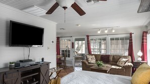 A spacious room with a large bed, a sofa, a TV, and a ceiling fan. - My Little House | Hot Tub | Shared Pool (Fredericksburg)
