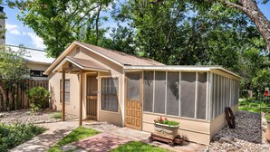 A house with a screened porch, a front door, and a small garden area with a potted plant. - My Little House | Hot Tub | Shared Pool (Fredericksburg)