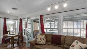 A cozy living room with a brown sofa, a wooden dining table, and red curtains. - My Little House | Hot Tub | Shared Pool (Fredericksburg)