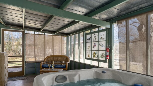 A spa area with a hot tub, wicker furniture, and large windows with artwork. - My Little House | Hot Tub | Shared Pool (Fredericksburg)