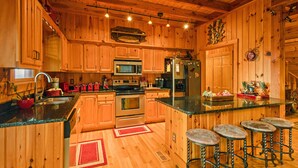 A wooden cabin-style kitchen with a central island, stainless steel appliances, and a bar area with stools. - Family Cabin With Mountain Views (Boone)